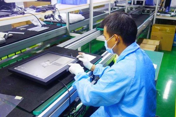 Technician testing a medical display monitor on a production line.