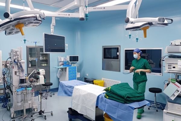 Modern blue operating room with medical staff preparing for surgery, equipped with ceiling-mounted medical displays and surgical lights