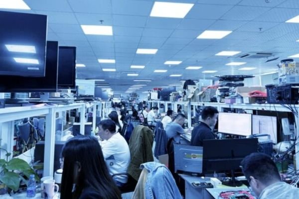 Área de fabricación y pruebas de monitores médicos con ingenieros y técnicos trabajando en líneas de producción e inspección